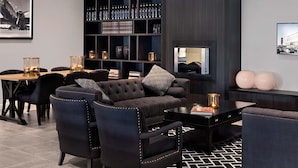 Un salon moderne avec un canapé de couleur sombre, des fauteuils assortis, une table basse, une bibliothèque avec des bouteilles et un tableau encadré au mur.