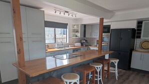 Una cocina con una isla de madera, taburetes de bar y un refrigerador.