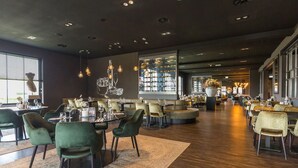 A spacious restaurant with multiple seating areas, including round tables and booths, and a large window providing natural light. - A Serene Dutch Getaway with Monastic Charm and Natural Surroundings! (Deurne)