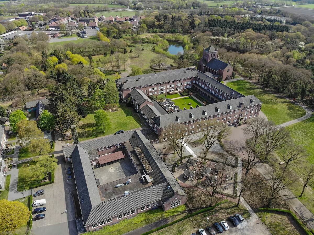 Een luchtbeeld van een grote campus met meerdere gebouwen, een centrale binnenplaats en omliggende groene zones.