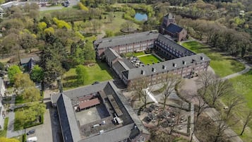 Een luchtbeeld van een grote campus met meerdere gebouwen, een centrale binnenplaats en omliggende groene zones.