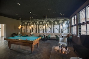 Ein Billardtisch, eine Sitzecke und ein Wandbild mit Statuen.