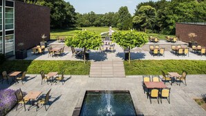 An outdoor patio with tables and chairs, a central fountain, and a brick building on the left. - A Great Place to Unwind and Explore! Close to Valkhof Museum! (Berg en Dal)