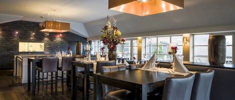 A modern dining area with a central table, surrounding chairs, and pendant lighting.