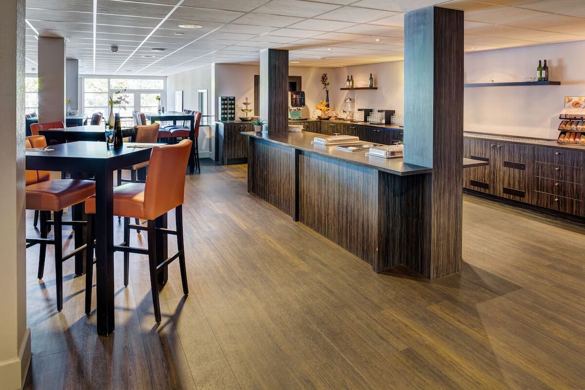 A modern bar area with wooden flooring, bar stools, and a counter with various items.