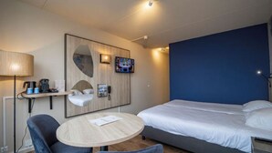 Ett hotellrum med en säng, ett runt bord, en stol, en tv, en lampa och en telefon som är monterad på väggen.
