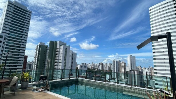 Una piscina sul tetto con poltrone relax, uno skyline cittadino sullo sfondo e moderni edifici.