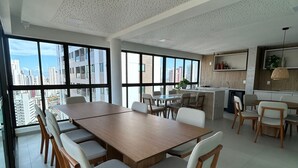 Zona pranzo moderna con un tavolo grande e sedie, una cucina sullo sfondo e ampie finestre con vista sulla città.