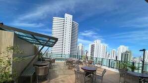 Una terrazza sul tetto con posti a sedere all'aperto, ringhiera in vetro e skyline urbano sullo sfondo.