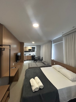 A hotel room with a bed, a desk, a TV, a kitchenette, and a dining area.