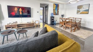 A modern living room with a flat-screen TV, a wooden dining table, and a sofa. - Welcoming 2-bedroom apartment with fitness room in Nairobi (Nairobi)
