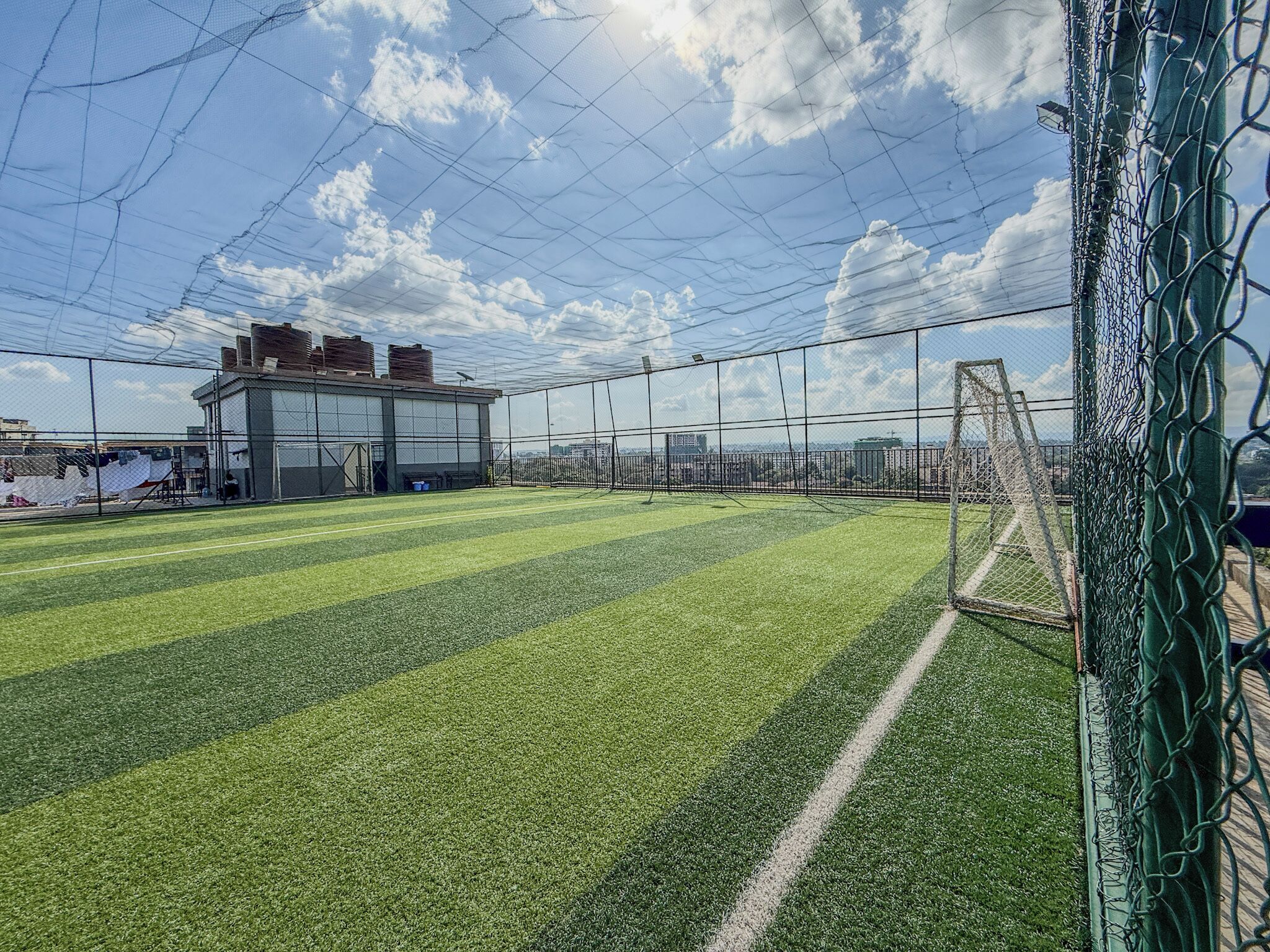 A sports field with a goalpost, surrounded by a chain-link fence, and a building in the background.