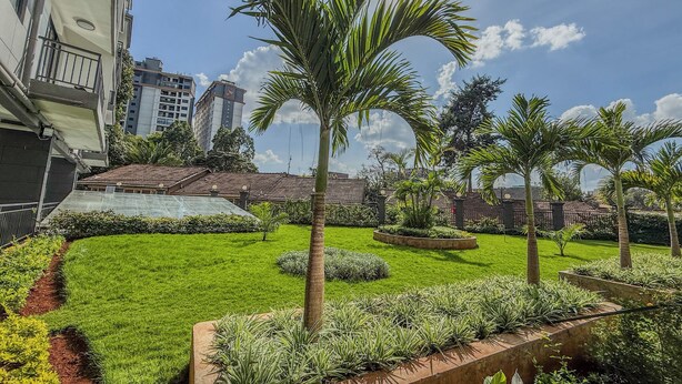 A well-maintained garden with palm trees, a grassy lawn, and a brick pathway. - Welcoming 2-bedroom apartment with fitness room in Nairobi (Nairobi)