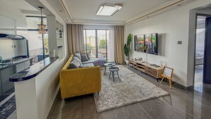 A modern living room with a sofa, TV, and a kitchen area. - Welcoming 2-bedroom apartment with fitness room in Nairobi (Nairobi)