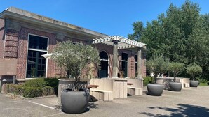 A brick building with large windows, a covered outdoor seating area, and large planters.