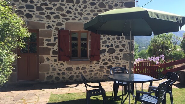 A stone building with a patio, a table with chairs, and an umbrella. - “Gîte Les Bannes” with Mountain View and Wi-Fi (Saint-Sauves-d'Auvergne)