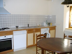 Una cocina con estufa, lavavajillas y lavadora, armarios de madera y una mesa de comedor redonda.