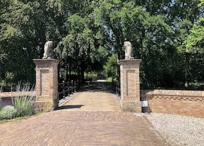 Un sendero pavimentado que atraviesa un arco de ladrillo con estatuas en la parte superior, rodeado de árboles y un borde de grava.