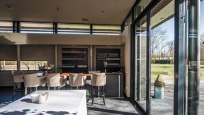 A modern dining area with a bar, bar stools, and a table set for two. - Sleep Peacefully in Scenic Room w/ Walking Trails Nearby (Renesse)