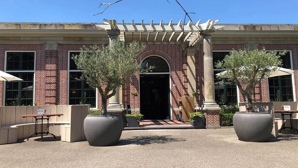 A building with a brick facade, a central entrance with an arch, and two large planters with trees. - Sleep Peacefully in Scenic Room w/ Walking Trails Nearby (Renesse)