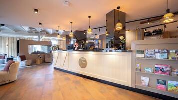 Een modern interieur met een receptiebalie, houten vloeren, hanglampen en een bar voorzien van boekenkasten en flessen.