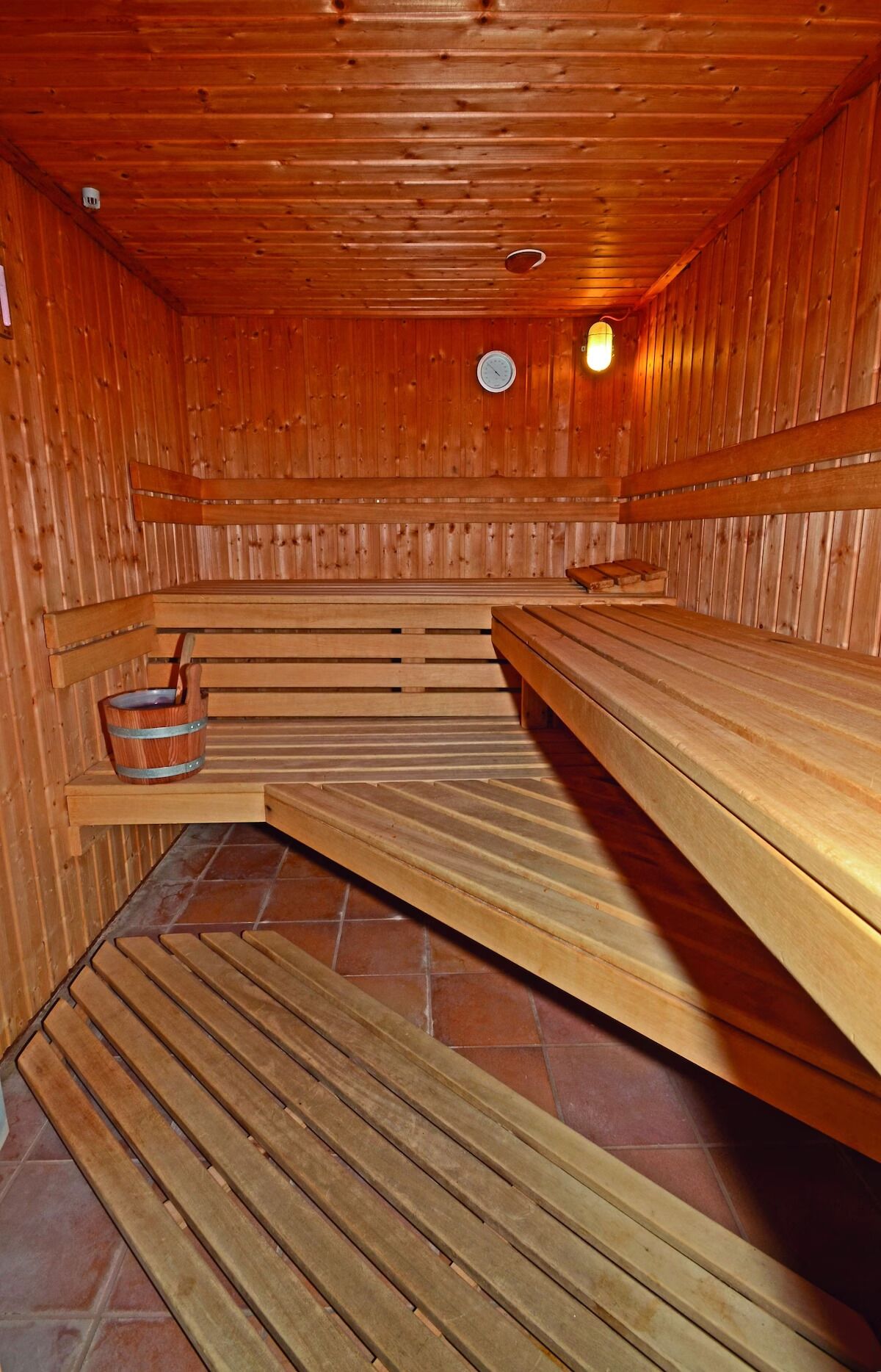 A sauna with wooden benches, a bucket, and a clock on the wall.