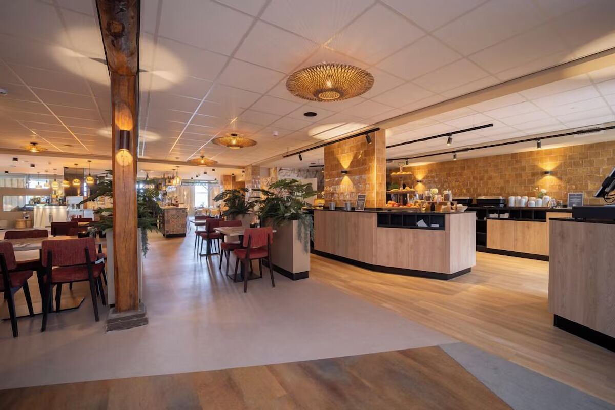 A spacious hotel lobby with wooden flooring, a central seating area, and a counter with a coffee station.