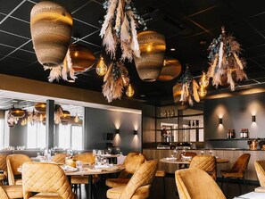 L’intérieur d’un restaurant, avec des luminaires suspendus, des chaises rembourrées et un coin bar.