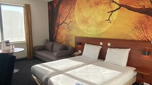 A hotel room with a bed, a sofa, a table, and a large wall mural of a tree and moon.