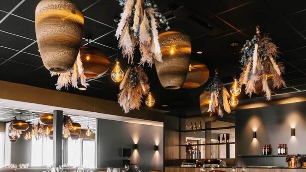 A restaurant interior with hanging light fixtures, cushioned chairs, and a bar area.
