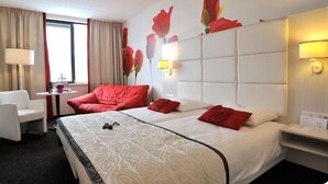A hotel room with a large bed, two bedside tables, a chair, a desk, and a window with curtains.