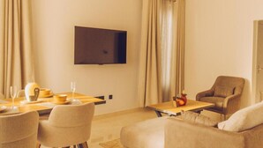 Uma sala de estar moderna com televisão de tela plana na parede, uma área de jantar com mesa e cadeiras, e um sofá.