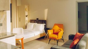 Quarto de hotel moderno com cama, escrivaninha, poltrona laranja, sofá e estante embutida.