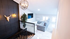 A staircase with a dark wall, a bull's head decoration, a chandelier, and a living room with a grey sofa and a TV. - Peaceful 3-bedroom apartment with AC in El Puig de Santa Maria (El Puig de Santa Maria)