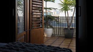 A room with a bed, a balcony with a view of palm trees and a fence, and a large potted plant. - Peaceful 3-bedroom apartment with AC in El Puig de Santa Maria (El Puig de Santa Maria)