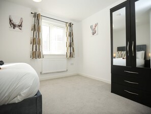 Ein Schlafzimmer mit einem Bett, einem Kleiderschrank, einem Heizkörper und zwei Wandbildern mit Schmetterlingen.