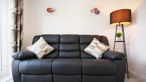 En svart lädersoffa med två dekorativa kuddar, en golvlampa och två väggdekorationer.