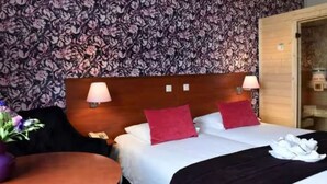 Une chambre d’hôtel avec un papier peint à motifs floraux, deux lits avec des oreillers rouges, une tête de lit en bois et une porte en bois.