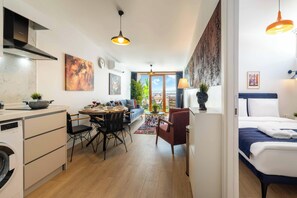 Eine moderne Küche mit integriertem Waschmaschinenanschluss, ein Essbereich mit Tisch und Stühlen, eine Couch und Blick ins Freie.