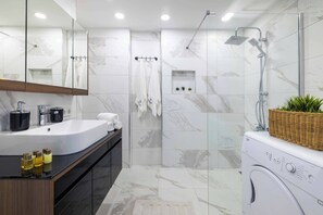 Ein modernes Badezimmer mit großem Spiegel, Waschbecken, Dusche und Waschmaschine.
