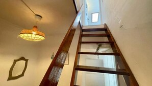 A wooden interior staircase with a handrail, a hanging light fixture, and a door at the top. - Maria (Lisbon)