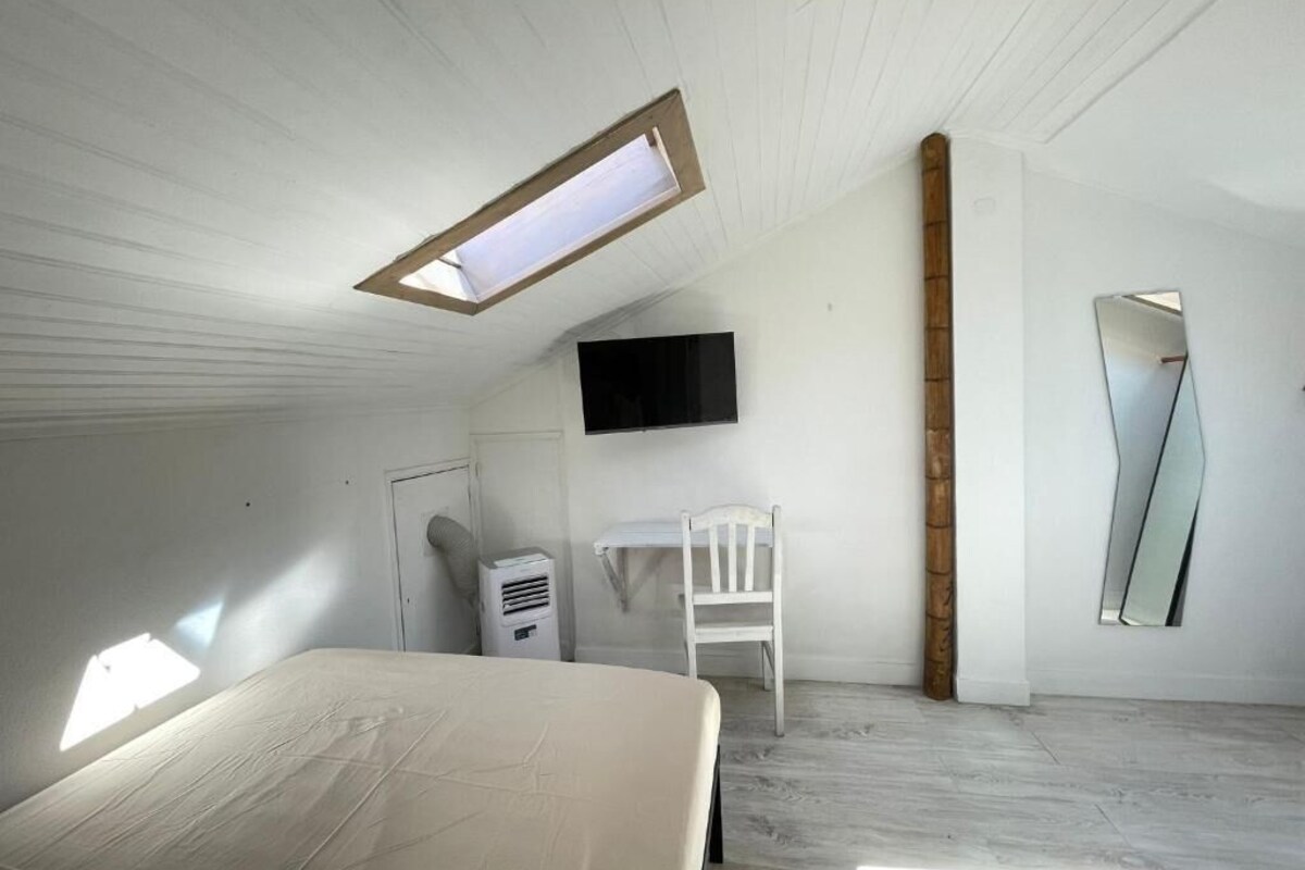 A bedroom with a bed, a desk, a chair, a TV, and a skylight.