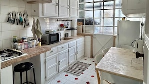 A kitchen with white cabinets, a stove, a microwave, and a dining area with a table and chairs. - Maria (Lisbon)