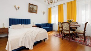 A bedroom with a bed, a blue sofa, a dining table with chairs, and a chandelier. - Cozy Studio by the Market Square | Fountain Park (Warszawa)