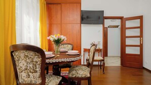 A dining area with a round table, floral chairs, a vase with flowers, and a television on the wall. - Cozy Studio by the Market Square | Fountain Park (Warszawa)