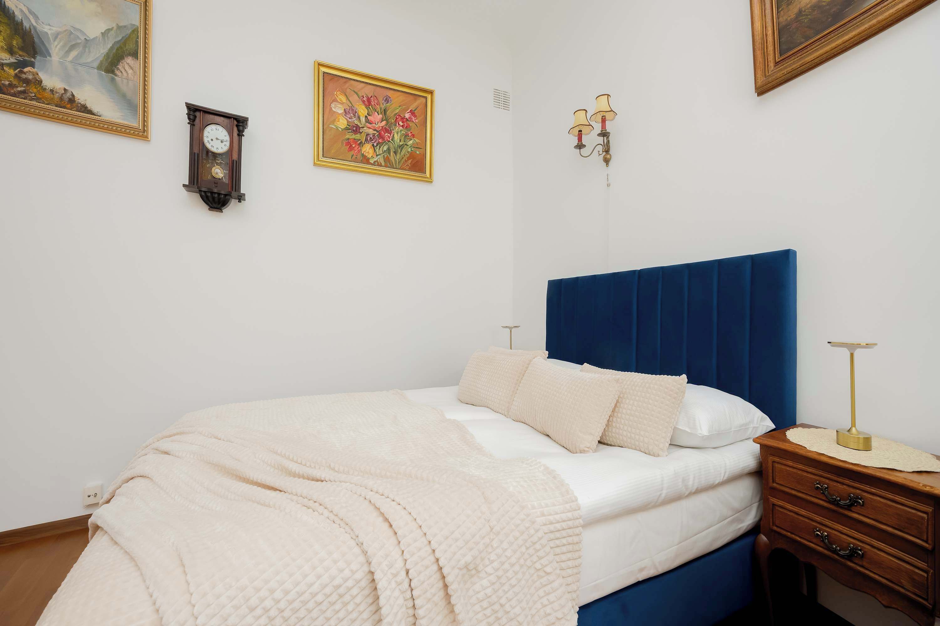 Een slaapkamer met een bed, nachtkastje en een klok aan de muur.