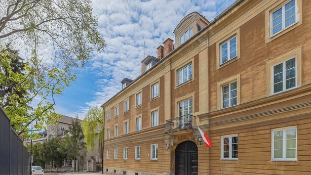 A historic building with a stone-paved street, a black gate, and a red sign. - Cozy Studio by the Market Square | Fountain Park (Warszawa)