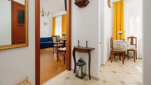 A hallway with a mirror, a wooden door, a dining area with a table and chairs, and a blue sofa in the background. - Cozy Studio by the Market Square | Fountain Park (Warszawa)