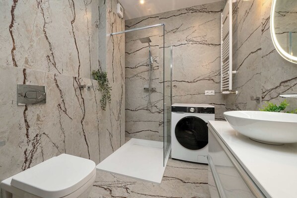 Un baño moderno con ducha envuelta en vidrio, lavadora integrada y un lavamanos grande.