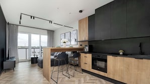 Une cuisine moderne avec un parquet disposé en motif chevron, un îlot central en bois et une grande fenêtre donnant sur un paysage urbain.